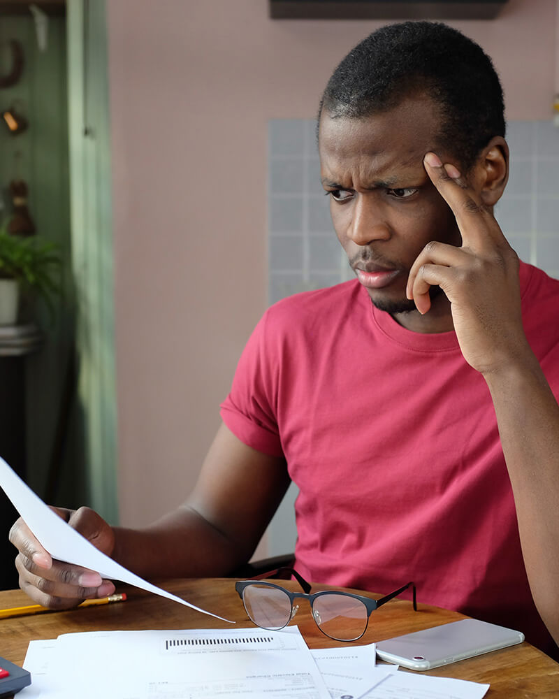 A man frowning at an official government letter at his kitchen table.