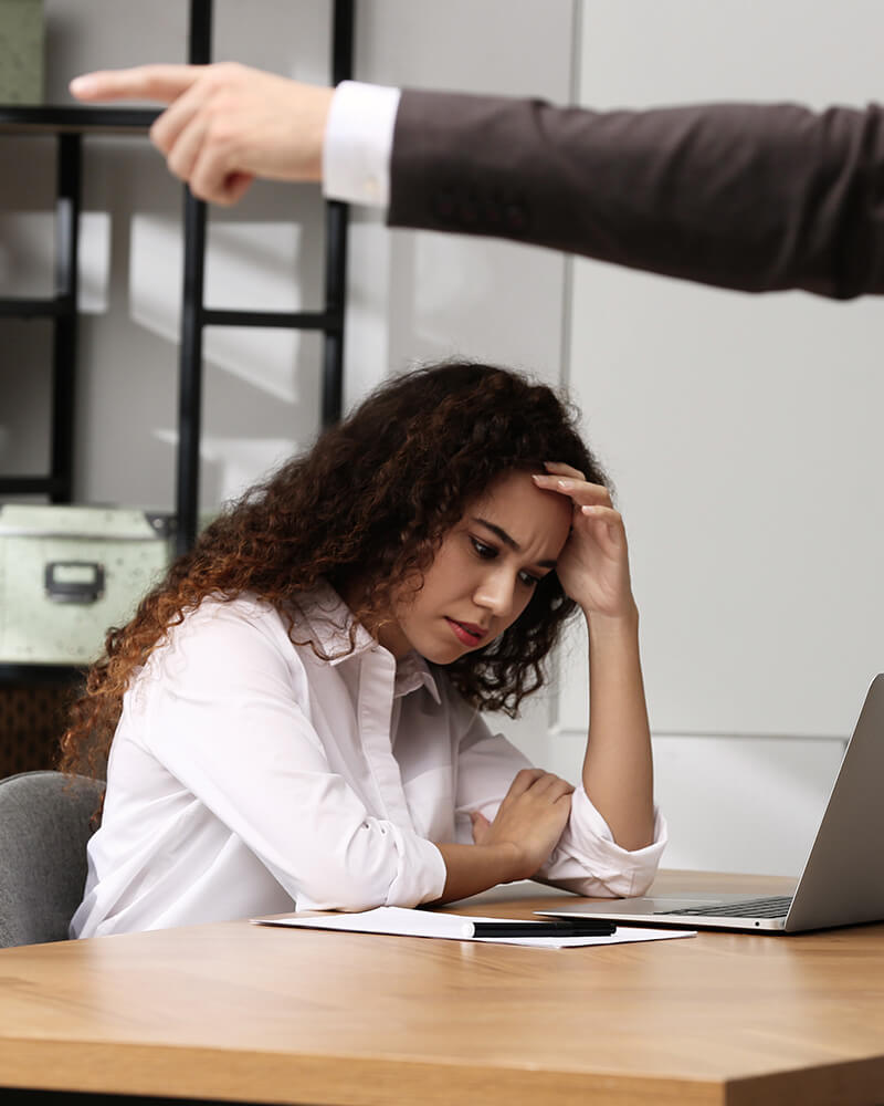 A woman at her desk looking distressed while a manager points at her.